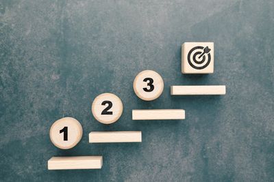 Wooden blocks numbered 1 to 3 and a target symbol on steps against a dark background.