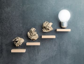 Steps of progress with crumpled paper and a light bulb.