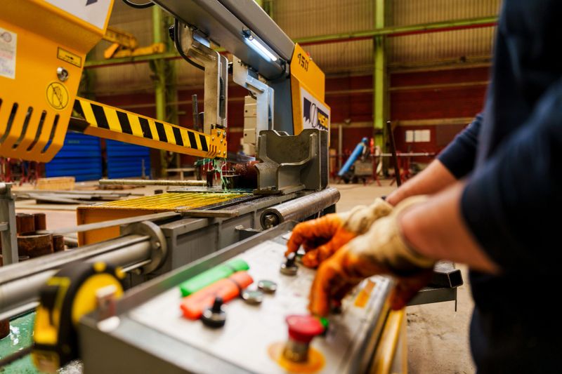 A man operates a CNC machine which engraves metal while working in a manufacturing and fabrication facility.
