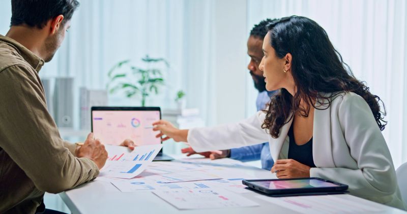 Group of business professionals meeting discussing financial strategy reviewing data on laptops and documents for market analysis at office. Finance meeting concept.