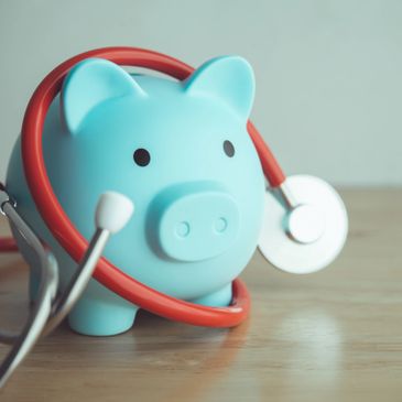 Blue piggy bank with red stethoscope on a wooden table.