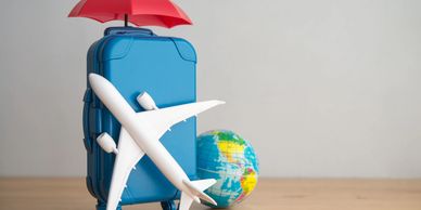 Miniature travel setup with plane, suitcase, umbrella, and globe.