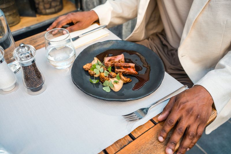 Overhead composition of an upscale restaurant table featuring a beautifully plated gourmet meal on matte black ceramic plate, accompanied by crystal stemware and refined table settings.