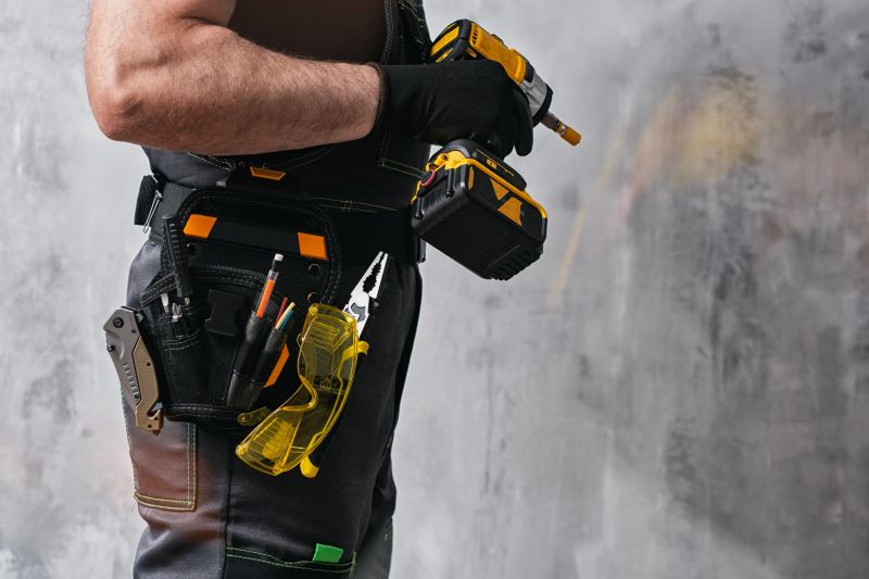 Uniformed construction worker holding a yellow colored cordless screwdriver with a set of tools on his belt. The concept of repair, maintenance and electrical installation