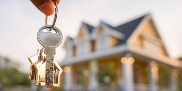 Hand holding house-shaped keychain in front of a house.