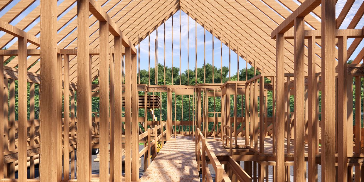 Wooden house frame under construction with clear sky and trees in background.