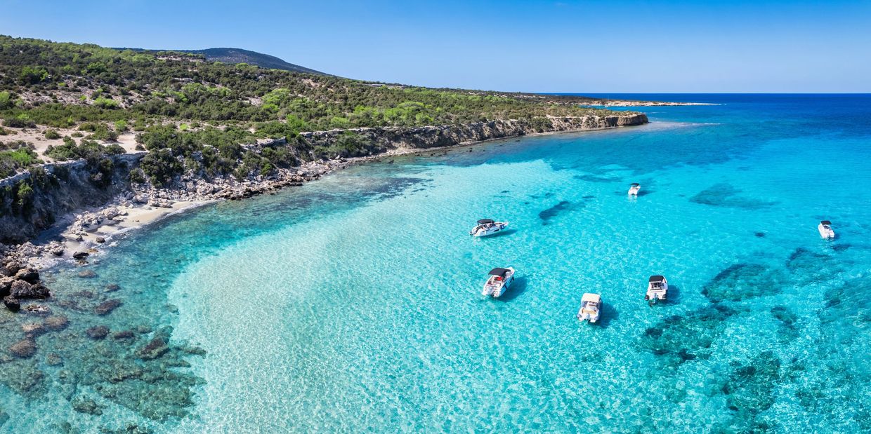 Clear blue waters with boats near a rocky coast.