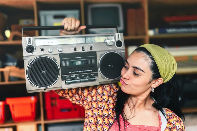 young happy woman carrying retro tape recorder on shoulder indoors