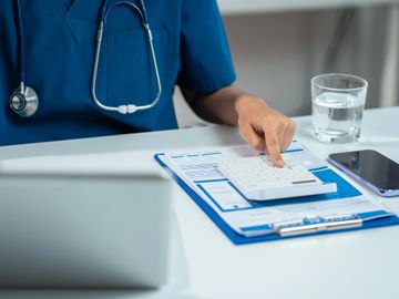 Healthcare professional using calculator and clipboard at desk.