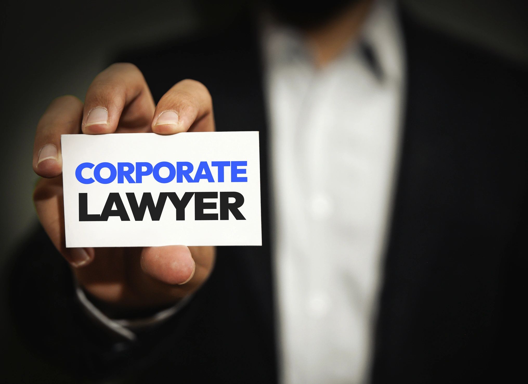Lawyer wearing a suit holding up a business card that says CORPORATE LAWYER.
