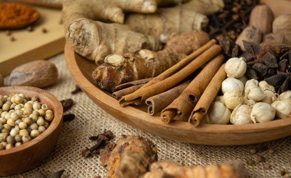 A wooden bowl filled with various spices including cinnamon sticks and dried seeds.