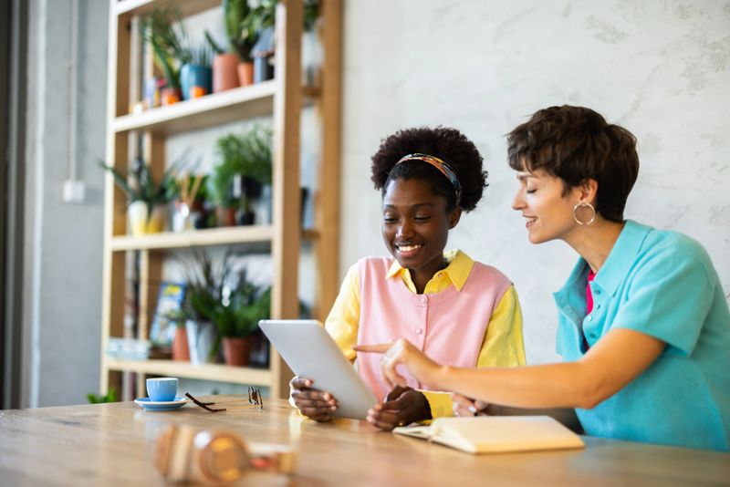 Two young women entrepreneurs are working together, using a digital tablet, in a bright and modern office space