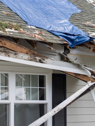 Snow-damaged roof with a blue tarp covering the broken section.