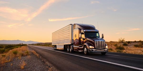 A large semi-truck driving on a desert highway at sunset.