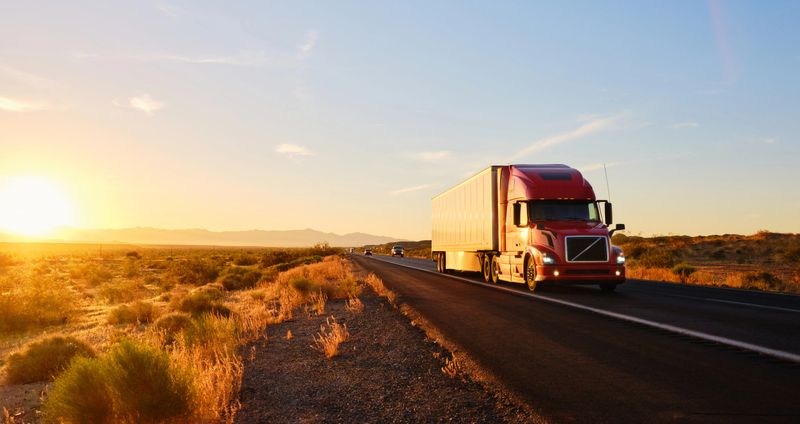 Large semi truck hauling freight on the open highway in the western USA under a morning sky.