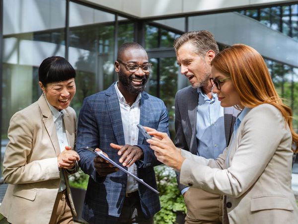 Four professionals happily discussing business outside a modern office building.
