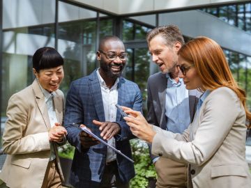 Four professionals engaged in a lively discussion around a tablet outdoors.