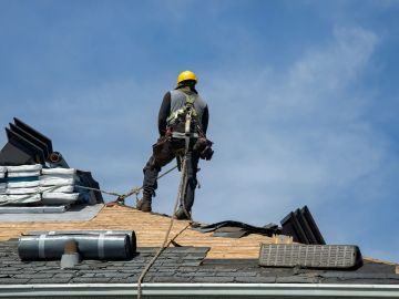 Roofer working on a roof with safety harness and gear.