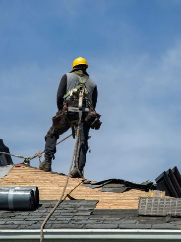 Construction worker in safety gear working on a roof under clear sky.