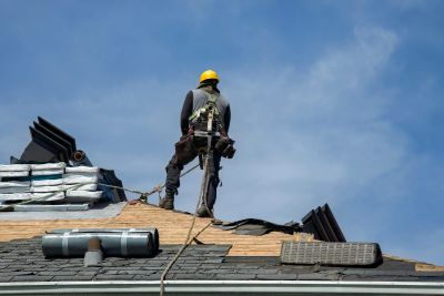 Construction worker standing on a roof under blue sky.