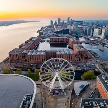 A cityscape with a large Ferris wheel near a river at sunset.