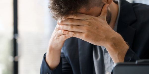 Stressed businessman covering face at desk with documents and pen.