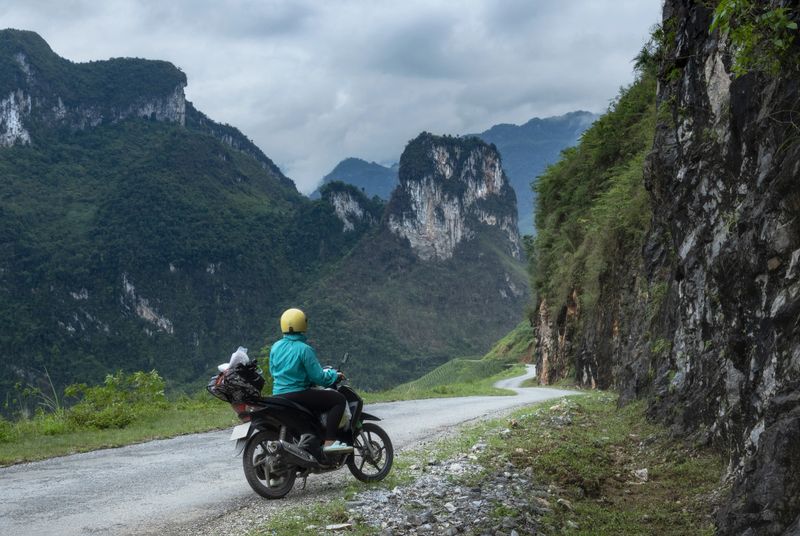 Solo female biker at the side of a winding road enjoying the scenery of magnificent karst mountains landscape on Ha Giang loop