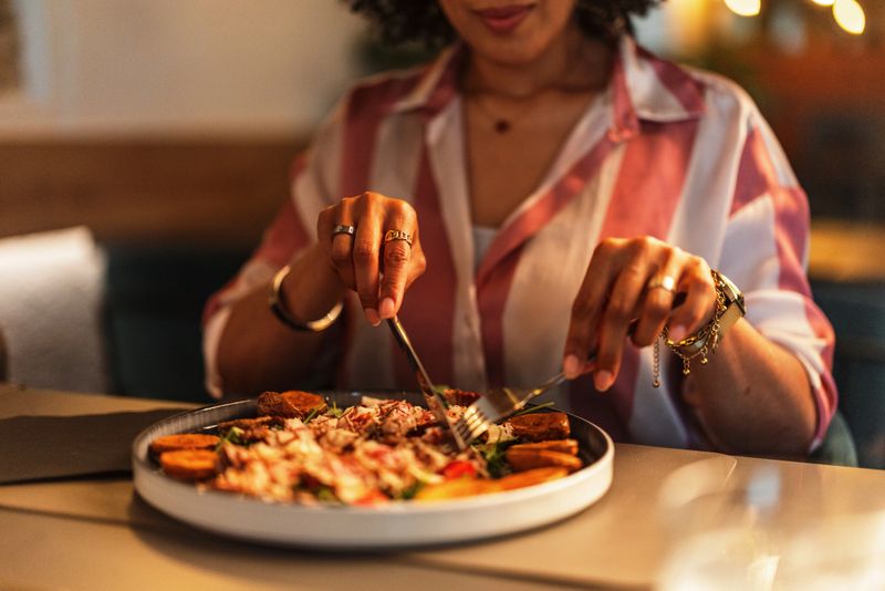 A woman delicately uses a knife and fork to enjoy a gourmet meal, creating an elegant fine dining experience. The setting is warm and inviting, reflecting a sophisticated culinary atmosphere.