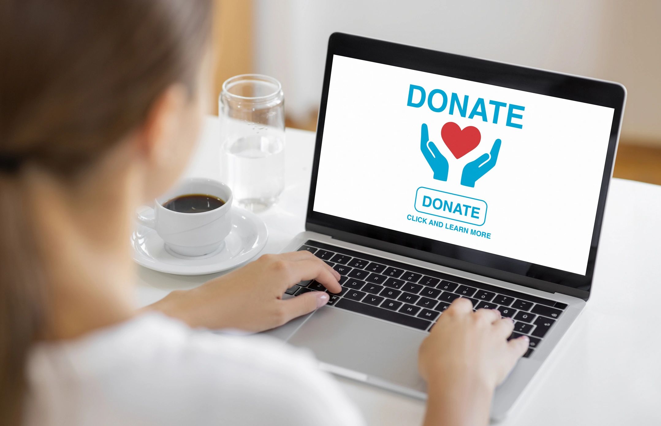 Person using a laptop to donate online with coffee and water nearby.