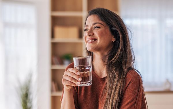 Smiling woman holding a glass of water indoors.