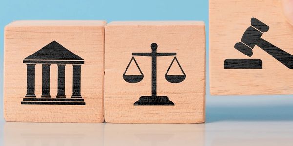 Wooden blocks with legal symbols: courthouse, scales of justice, and gavel.