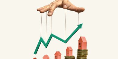 Hand manipulating a rising green arrow over houses on coin stacks.