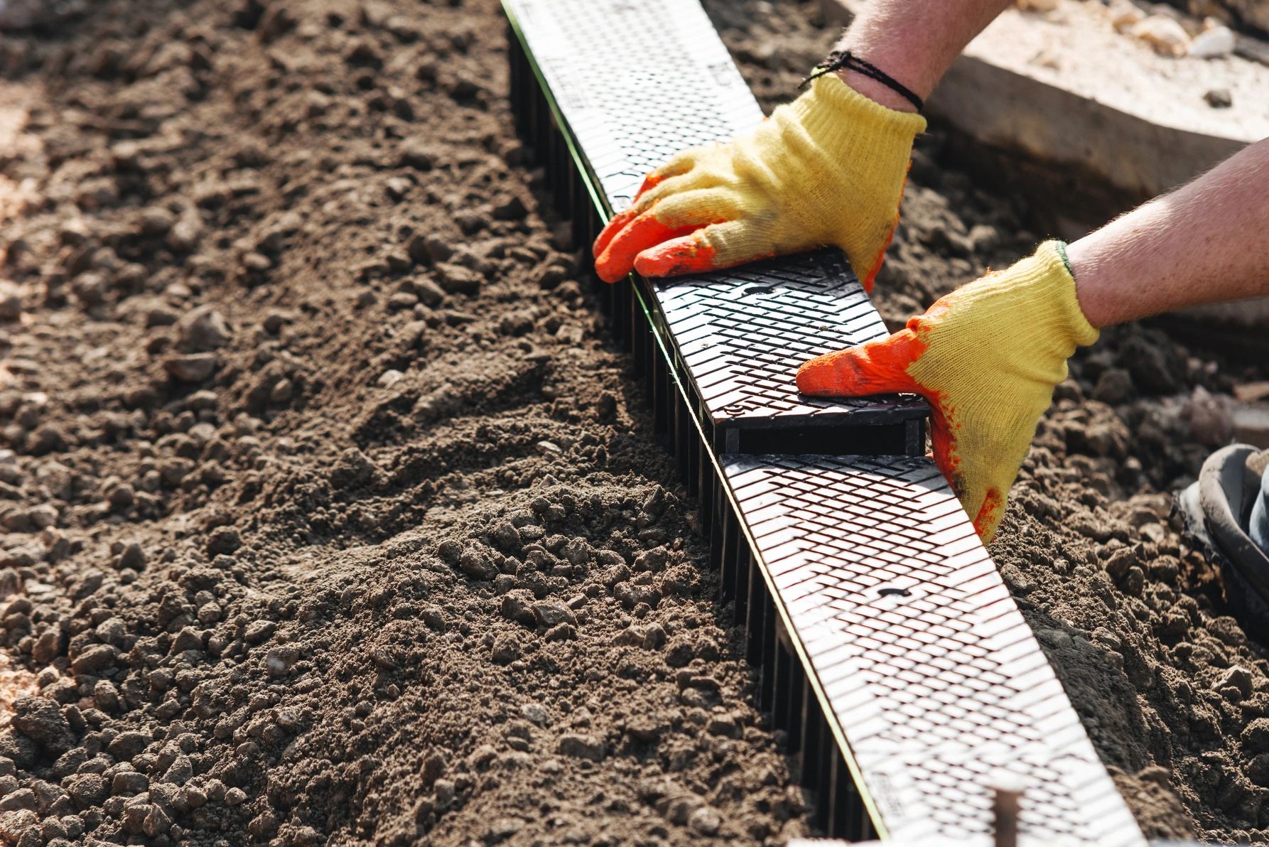 Hands in gloves installing a plastic garden edge in soil.