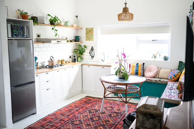 Bright, modern kitchen with white cabinets, subway tile backsplash, a patterned rug, and various plants and decorative items.