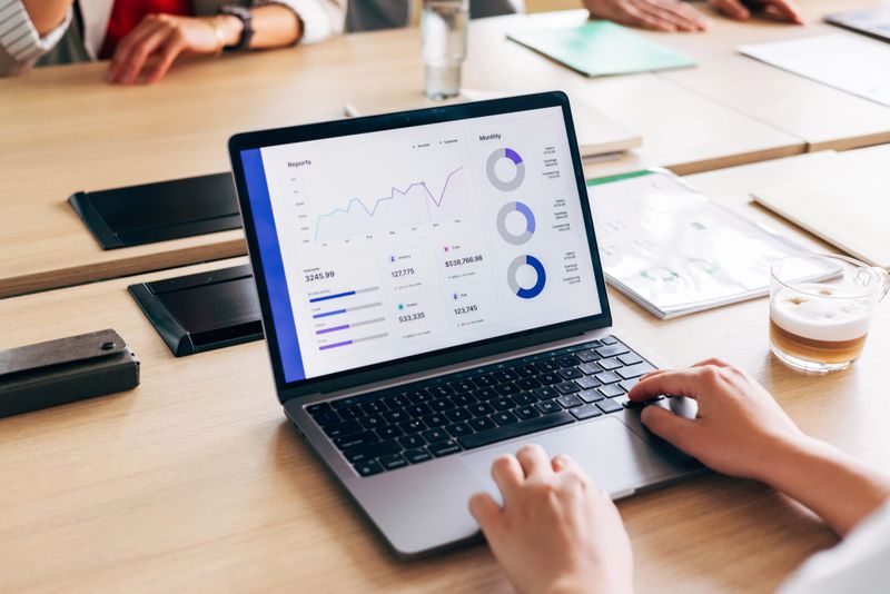 A close-up view of a person using a laptop to analyze data reports during a business meeting. Graphs and numerical metrics are displayed on the screen, emphasizing modern data analysis and presentation.