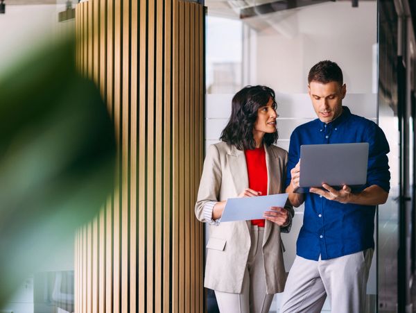 Two colleagues discussing work with documents and a laptop in a modern office.