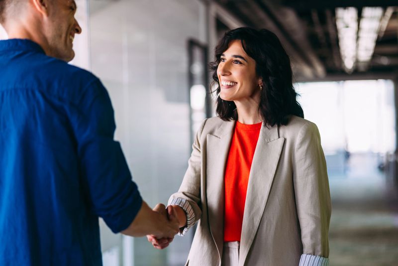 Two well-dressed business professionals are engaged in a positive handshake, symbolizing a successful agreement. The modern office background emphasizes teamwork, professionalism, and collaboration in the workplace.
