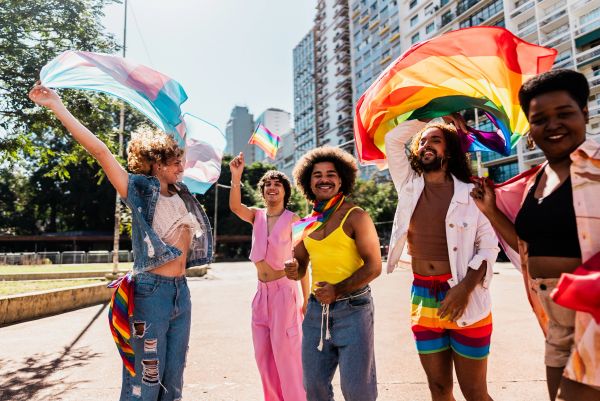 Group celebrating LGBTQ+ pride outdoors with colorful flags.