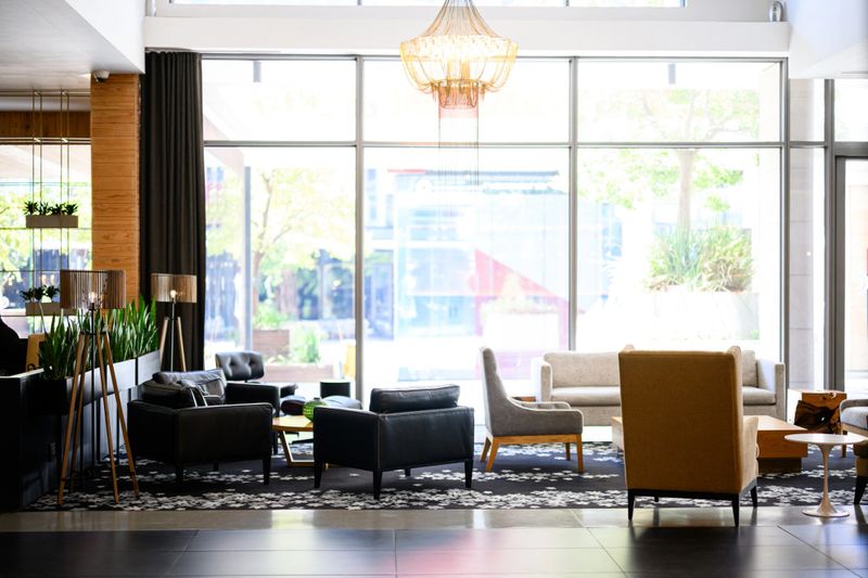 Spacious and luxurious hotel lobby with comfortable armchairs, a large window casting natural light, and an elegant golden chandelier.