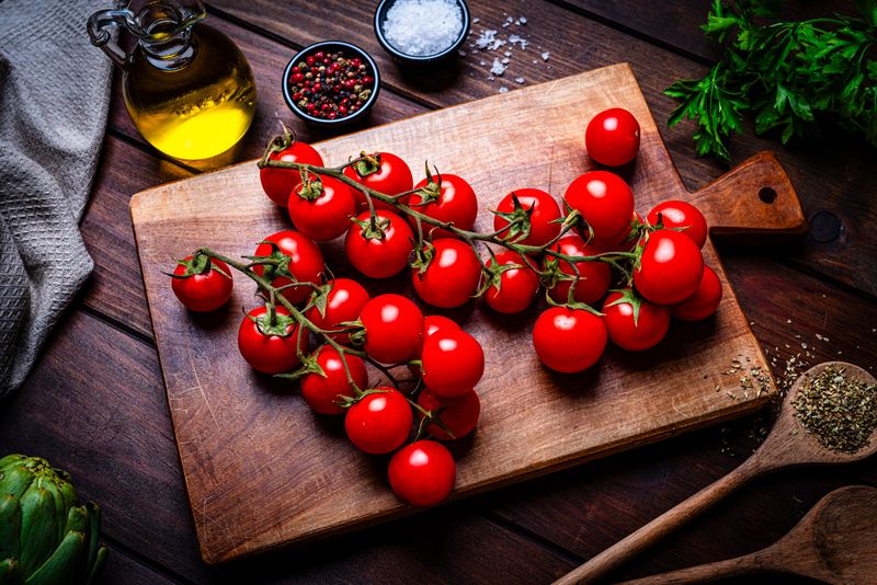 Ripe organic cherry tomatoes shot from above on a cutting board. Healthy vegetable diet, Mediterranean food, olive oil, pepper and salt. Juicy vegetarian food on wood table