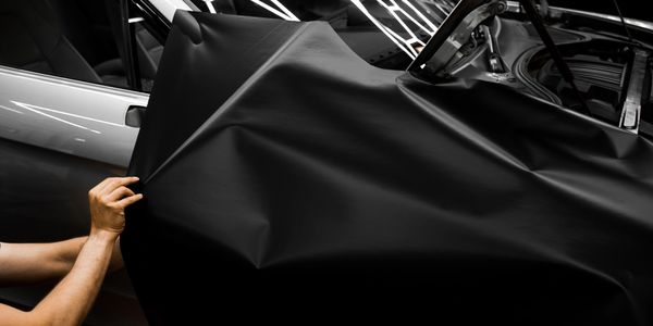 Person applying black vinyl wrap on a car.