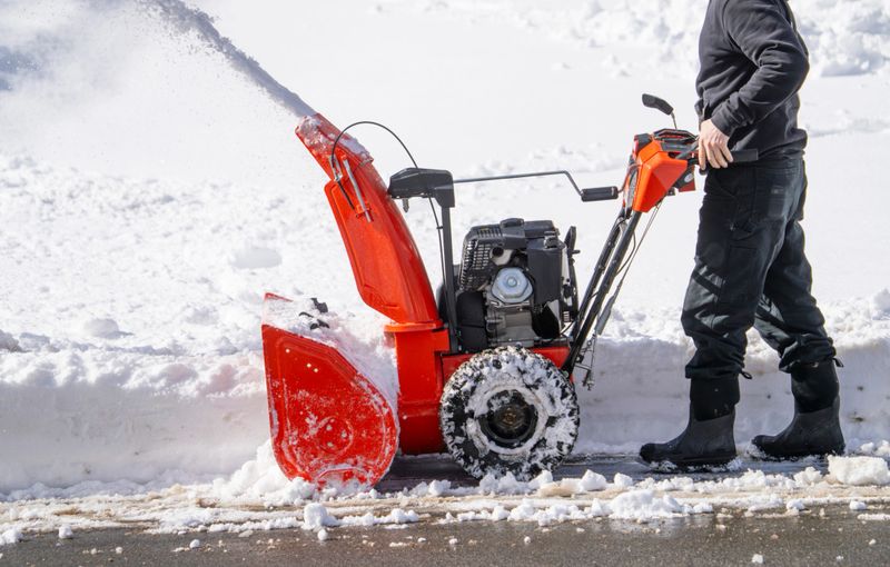 man removing snow on the driveway of the house by snow blower
