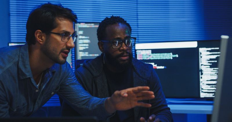 Black and Hispanic male engineers programmers work together collaborate discuss software development strategies in tech office late into the night. Software developer, artificial intelligence concept.