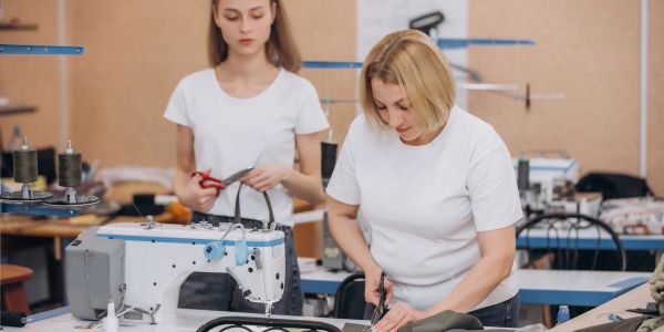 Two women working with fabric and scissors in a sewing workshop.