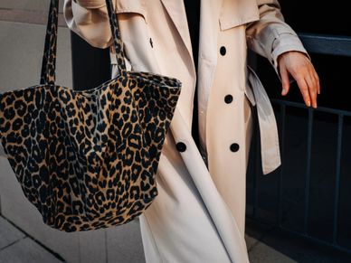 Person wearing a beige trench coat carrying a leopard print tote bag.