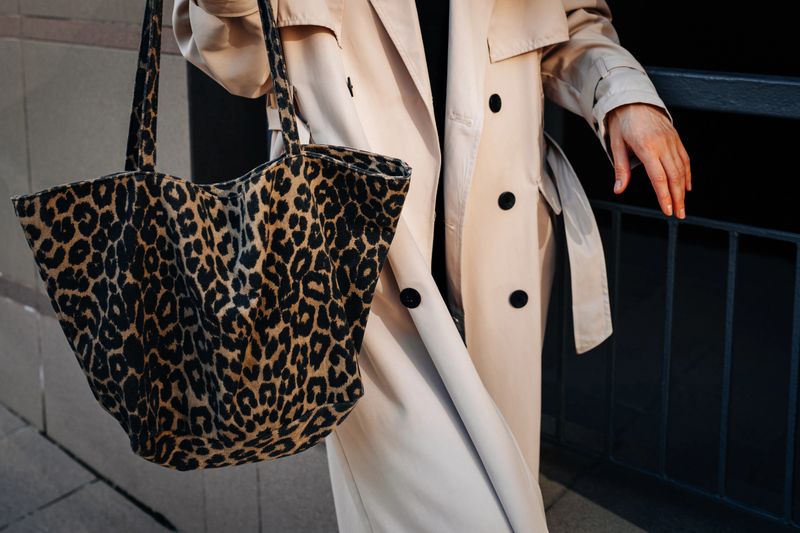 Street style details of modern trendy beige raincoat and leopard textile shopper, woman walking in city