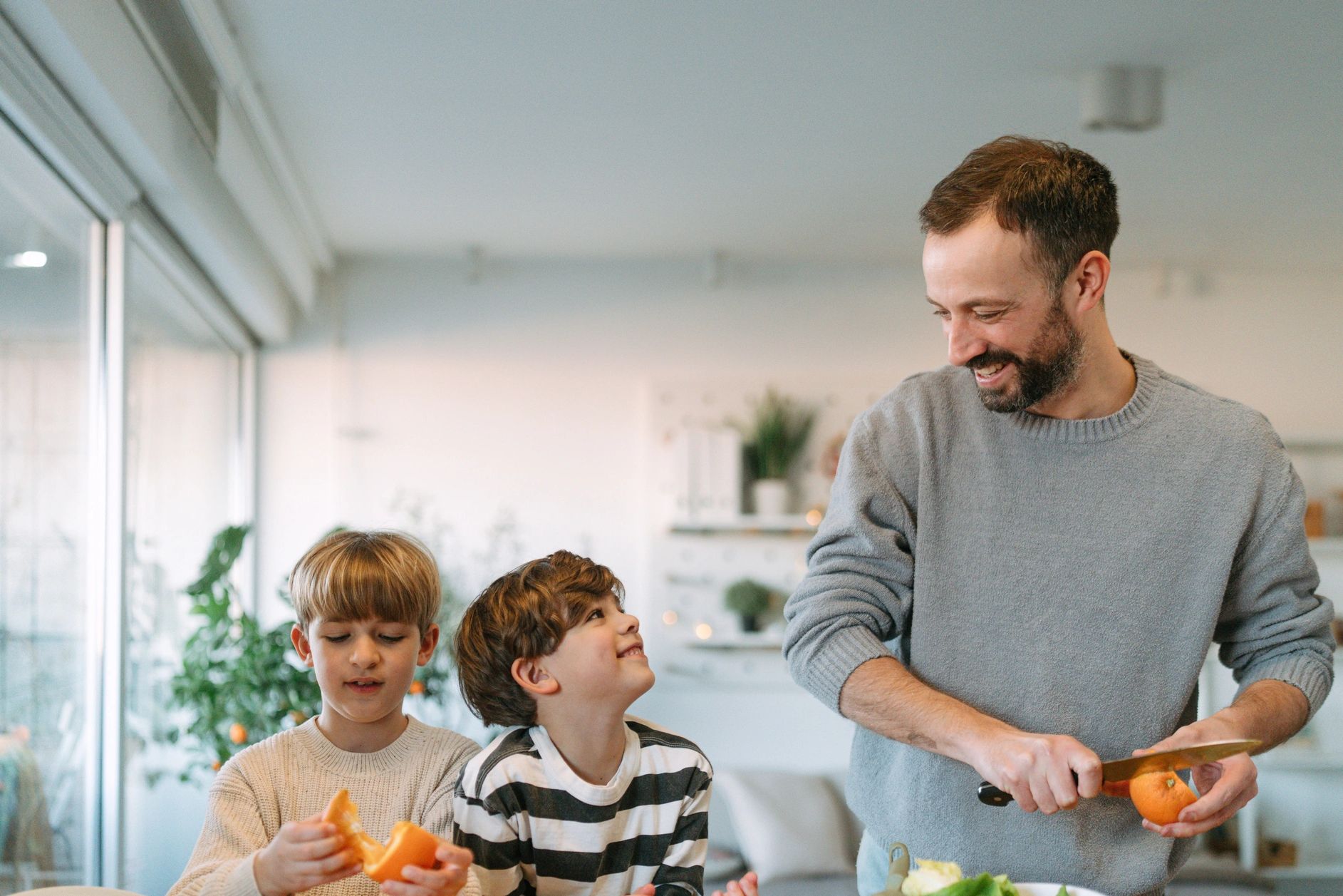 Father and two boys preparing food and peeling oranges.