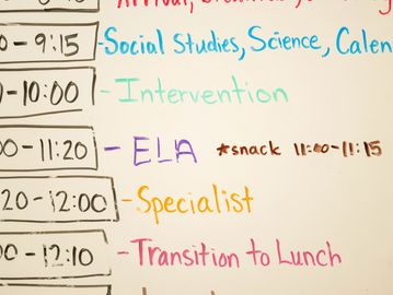 A colorful classroom schedule with subjects and times written on a whiteboard.