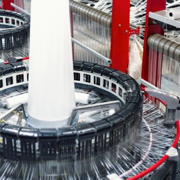 A textile machine weaving white fabric with intricate thread arrangement.