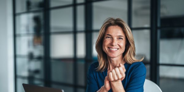 Smiling woman sitting at desk with laptop in modern office.